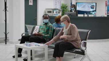 Multiethnic group of patients sitting in hospital reception to attend medical exam for covid 19 prevention. People with face mask having consultation appointment during coronavirus epidemic.