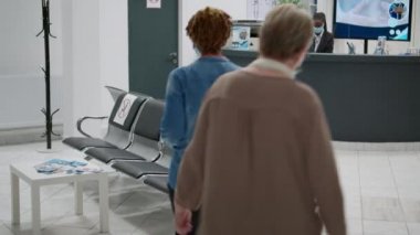 Covid 19 salgını sırasında hastane resepsiyonunda check-up randevusuna giden çeşitli hastalar. Yüz maskeli insanlar bekleme salonunda oturup pratisyen hekimle tıbbi danışmaya başlıyorlar..