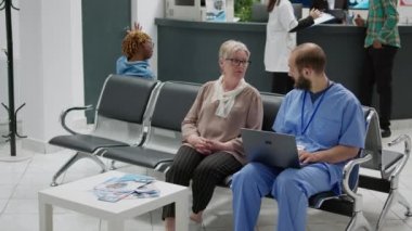 Hastane resepsiyonunda dizüstü bilgisayara bakan kıdemli kadın ve tıp asistanı, hastalık teşhisi ve tedavi hakkında konuşuyorlar. Hasta ve hemşire bekleme salonunda iyileşme hakkında konuşuyorlar..