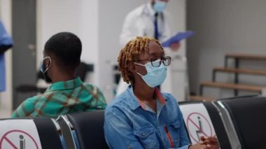 Yüz maskeli bir kadın hasta bekleme odasında oturuyor, hastane resepsiyonunda uzman doktorla görüşüyor. Covid 19 salgını sırasında check-up 'a katılan kadın.
