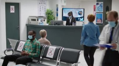 Multiethnic group of people sitting in waiting area during covid 19 pandemic, having checkup visit appointment with medical specialist. Patients with face masks attending prevention exam.