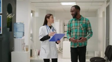 Tıbbi asistan, Afrika kökenli Amerikalı hastaya röntgen taraması sonuçlarını açıklıyor. Hastanenin bekleme salonunda dizüstü bilgisayarla yapılan radyografi teşhisinden bahsediyor. Çeşitli insanlar hastalıklardan bahseder..