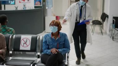 General practitioner inviting patient in medical office for checkup visit, waiting in hospital reception during coronavirus pandemic. Doctor and woman with face mask doing consultation at clinic.