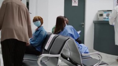 Senior woman with face mask attending checkup appointment with doctor in hospital reception facility. Patient doing consultation with medic at clinic during coronavirus epidemic.