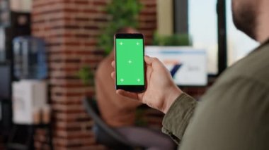 Cep telefonunda izole edilmiş yeşil ekran kullanan yeni başlayan işçiler, telif alanı arka planına sahip boş model görüntülere bakıyorlar. Modern akıllı telefon ekranında krom anahtar şablonu analiz ediliyor.