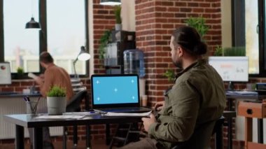Businessman looking at greenscreen on wireless laptop in company office, using computer with mockup template on display. Working on pc with isolated copyspace and blank chroma key.