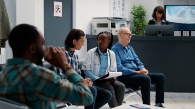 Bekleme alanında Asyalı bir hastayla konuşan Afrikalı Amerikalı bir doktor hastane resepsiyonunun lobisinde tıbbi personelle konsültasyon yapıyor. Bekleme odasında çeşitli insanlar sohbet ediyor..