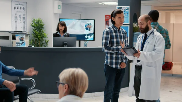 Asian patient discussing with physician about diagnosis and treatment, talking in waiting room lobby at hospital reception area. Healthcare appointment for checkup visit consultation.