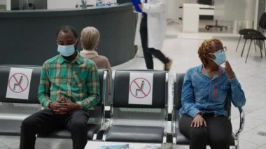 African american people waiting in hospital reception to attend checkup visit with medic during coronavirus pandemic. Patients with face mask sitting in waiting area before consultation.