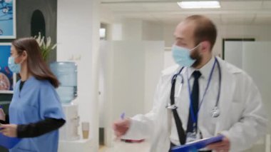 African american woman talking to physician at hospital reception during covid 19 pandemic. Diverse people with face masks doing consultation about coronavirus prevetion in waiting area.