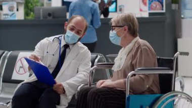 Doctor explaining disease diagnosis to woman with physical impairment, doing checkup consultation. Female wheelchair user suffering from chronic disability during coronavirus pandemic.