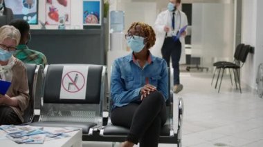 Yüzü maskeli Afrikalı Amerikalı bir kadın covid 19 salgını sırasında doktorla görüşmek için bekliyor. Coronavirus önleme ve tıbbi koruma için kontrol ziyareti yapıyor..