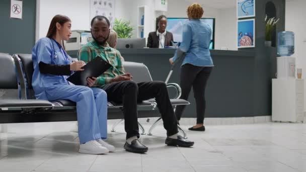 Eine Afroamerikanische Patientin Und Eine Krankenschwester Sprechen Der Wartezimmer Lobby — Stockvideo