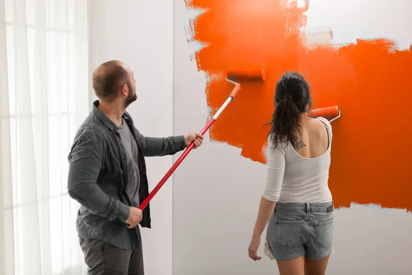 Young family painting with orange paint using roller paintbrush dipped in vibrant color. Home during renovation, decoration tools and equipment to renovate apartment walls with brush.