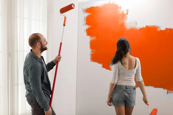 Confident Couple Painting Orange Paint Using Roller Paintbrush Dipped Vibrant — Stockfoto