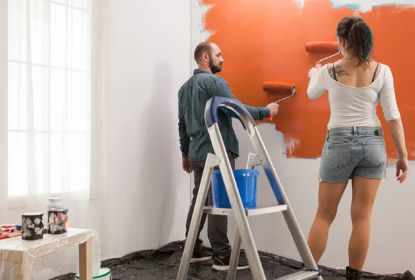 Young Couple Painting Walls Orange Color Using Renocating Equipment Ladder — 스톡 사진