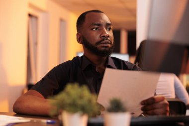 Ofisteki bilgisayarı kullanarak evrak raporuna çözüm bulmak için araştırma belgelerine bakan Afrikalı Amerikalı bir serbest yazar. Gün batımında dosyalardaki kurumsal bilgiler analiz ediliyor.