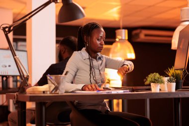 Proje yöneticisi yoğun zamanlamayı kontrol etmek için saate bakıyor, bilgisayar verileriyle raporun son teslim tarihi üzerinde çalışıyor. Kol saati kontrol ediliyor, mesai bitimi ve ofis işi..