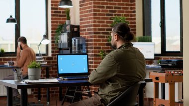 Şirket ofisindeki kablosuz bilgisayardan yeşil ekrana bakan bir işadamı, ekranda model şablonu olan bir bilgisayar kullanıyor. İzole edilmiş telif alanı ve boş renk anahtarı ile pc üzerinde çalışıyorum.