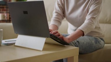 Evdeki kanepede oturup dizüstü bilgisayarla çalışan heyecanlı genç bir kadın. İçten gülümseyen genç Asyalı, evdeki taşınabilir bilgisayarda uzaktan kumanda yapıyor..