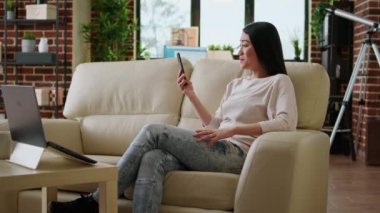 Smiling heartily woman discussing with work colleague on phone video call while working remotely. Happy asian freelancer on smartphone video call talking with client about job description.