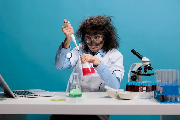 Mad scientist with wild appearance acting silly after lab explosion. Portrait of crazy amusing chemist acting funny and having dirty face and messy hair while sitting at desk and looking at camera