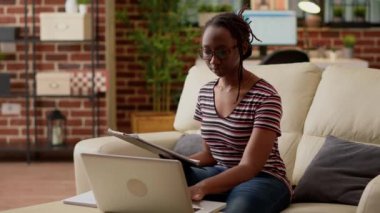 Company employee using laptop and paperwork to do remote job, browsing internet to work remotely on startup business. Young adult working from home on computer with online network.