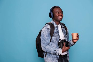 DSLR cihazı ve kablosuz kulaklık takan fotoğraf meraklısı şehir tatiline çıkıyor. Profesyonel kameralı ve sırt çantalı gülümseyen genç adam tatile çıkıyor..