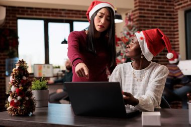 Çeşitli kadınlar festival iş ofisinde takım çalışması yapıyor, başlangıç raporları üzerinde çalışmak için beyin fırtınası yapıyorlar. Yılbaşı ağacı süslemeleri ve süslemeleri ile iş yerinde dizüstü bilgisayarda çalışmak.