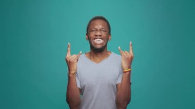 Süper havalı bir adam, rock metal işareti yapıyor, elleri kameranın önünde, eğlenceli punk müziğini pozitif enerjiyle ifade ediyor. Erkek hippi rockçı eğlence için şeytan boynuzu işareti yapıyor..