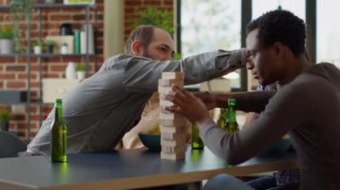 Multiethnic group of friends playing with cubes tower structure, having fun with wooden blocks on building. Cheerful people enjoying competitive activity with square pieces toy.