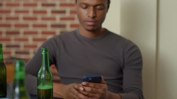 Hombre Afroamericano Navegando Por Internet Teléfono Móvil Sosteniendo Botella Cerveza — Vídeo de stock