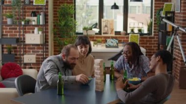 Diverse group of friends having fun with game activity, playing board games with wooden building tower on table. Men and women enjoying play with square blocks and pieces for entertainment.