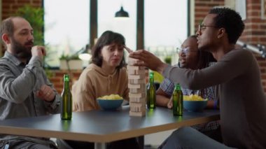 Men and women playing board games with tower cubes in living room, using square pieces and wooden blocks on building construction toy. Happy people having fun together. Tripod shot.