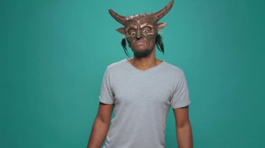 Young man wearing ancient tribal mask with sacral pattern and design, using artifact from indigenous antique history. Ceremonial native tribe artwork for magic mystic culture ritual.