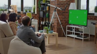 Oturma odasında yeşil ekranlı televizyon izleyen erkek ve kadınlar, izole edilmiş krom anahtar şablonu, kopya alanı ve boş arkaplan kullanıyor. Modern teknoloji TV ekranında. Üçayak atışı.