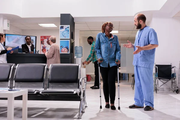 Young Woman Crutches Talking Male Nurse Medical Facility Lobby Waiting — Stockfoto