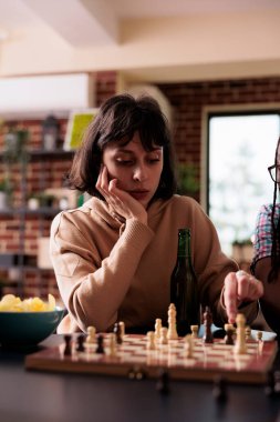 Bir sonraki satranç hamlesini düşünürken oturma odasında oturan düşünceli kadın. Akıllı tahta oyunu oyuncusu evde arkadaşlarıyla eğlenirken satranç tahtasının üzerinde bir parça oynatıyor..