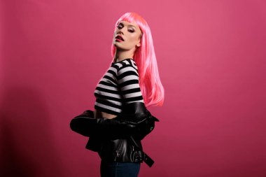 Portrait of beautiful lady looking at camera in studio, posing with natural leather jacket and pink hair. Attractive woman with punk rocker fashion style feeling carefree and sensual.