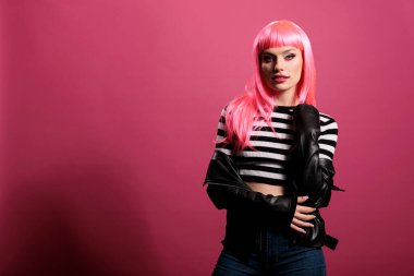 Confident punk woman wearing rocker leather jacket in studio, expressing carefree funky fashion style. Attractive beautiful lady with trendy clothes and stylish pink hair, cute makeup.