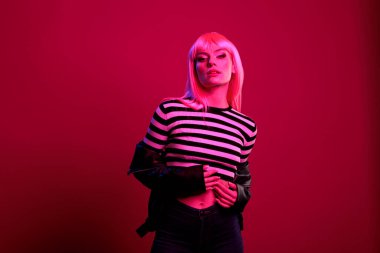 Deri ceketli, koyu renkli arka planda poz veren genç şehvetli bir yetişkin. Kamerada fotoğraf çekmek için pembe floresan ışıklandırma. Punk rock tarzıyla eğlenmek ve kendine güvenmek..