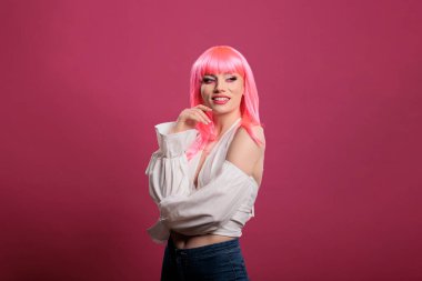 Kadın güzellik modelinin portresi kamerada samimi bir gülümseme, pembe saç peruğu ve modern güzel kıyafetler giyiyor. Güzel ve çekici hissetmek için şık bir moda ürünü, stüdyoda gülümsemek için..