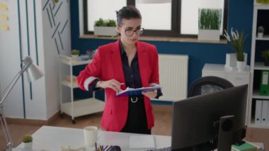 Executive assistant analyzing sales statistics on charts, looking through financial documents for new business strategy. Female employee planning development in startup office.