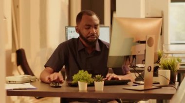 Bilgisayarda web sunumu planlayan Afrikalı Amerikalı bir adam, iş raporu oluşturmak için online araştırma bilgilerini kullanıyor. Ofisteki büyük pencereli sandık projesinde çalışıyor.