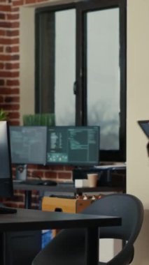 Vertical video Two software developers holding laptop with coding interface walking towards desk and sitting down talking about group project. Programmers team discussing algorithms pointing at
