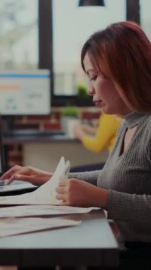 Dikey video: Ofis çalışanı başlangıç ofisinde liderlik sunumunu planlamak için belge ve dizüstü bilgisayar kullanıyor. Şirket çalışanı finansal kalkınma ve çevrimiçi ticaret için satış artışı üzerinde çalışıyor.