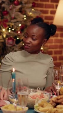 Dikey video: Mutlu Afrikalı Amerikalı kadın Noel yemeğinin tadını çıkarırken son sınıf öğrencisiyle konuşuyor. Çeşitli festival insanları kış tatilini Xmas 'ın içinde geleneksel yemekle kutluyor.