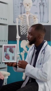 Dikey video: Kardiyoloji uzmanı kalp rahatsızlığı olan yaşlı bir hastaya tabletin kardiyogram test sonuçlarını gösteriyor. İyileşme tedavisini bulmak için kardiyovasküler ecg teşhisi