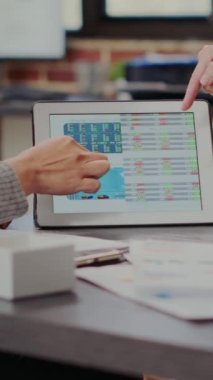 Dikey video: İş arkadaşları tablet üzerindeki borsa istatistiklerine bakıyor, iş projesini geliştiriyorlar. Satışları ve yatırım artışını dijital cihazdaki finansal grafiklerle analiz eden kadınlar. Kapat.