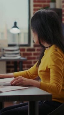 Vertical video: Consultant analyzing financial paperwork with sales graphs, working with laptop to develop marketing presentation for economy growth. Business woman creating successful strategy.
